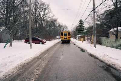 A school bus travels down a snowy suburban road lined with trees and homes in winter.