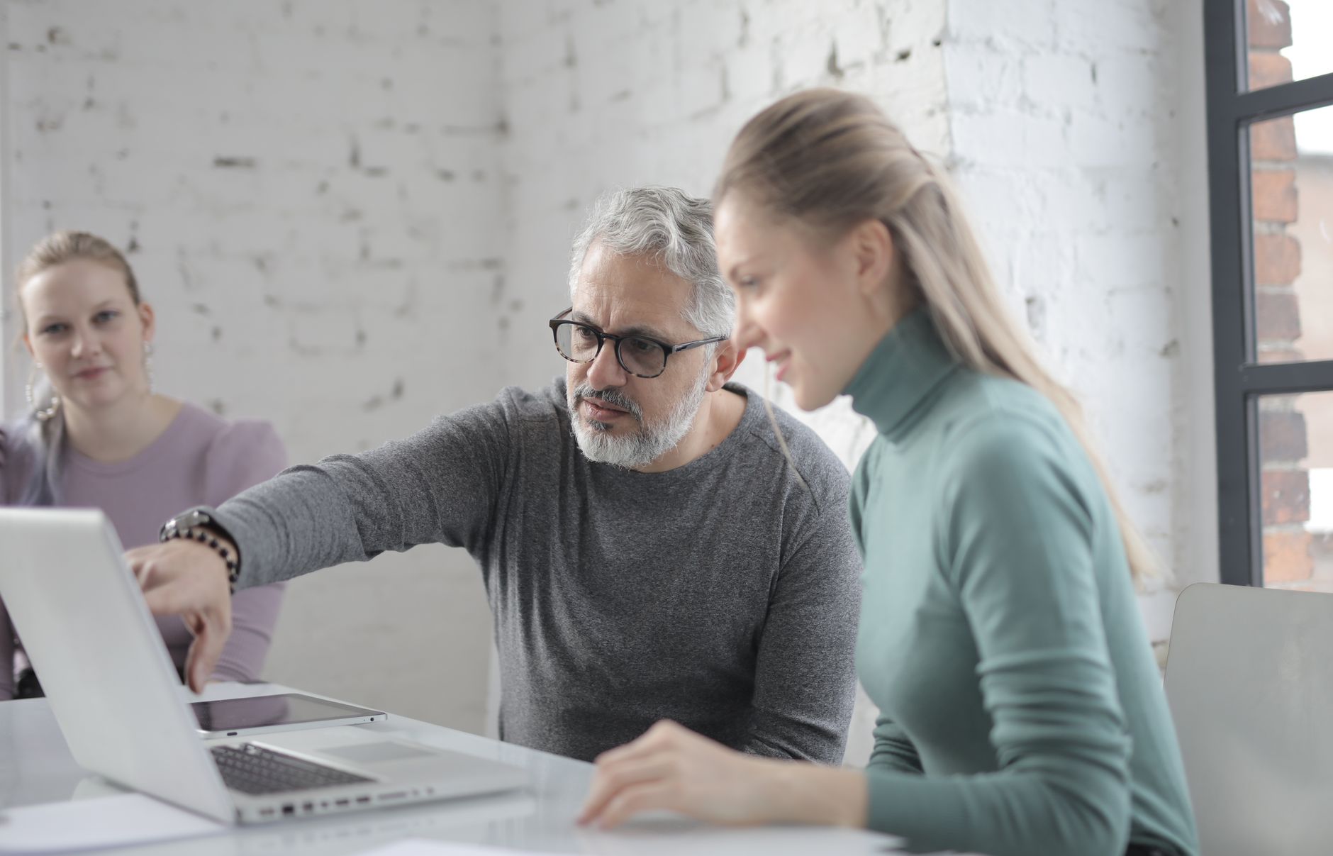 Concentrated middle aged man with coworkers sitting at table and working on project while explaining details to young female coworker during work in office
