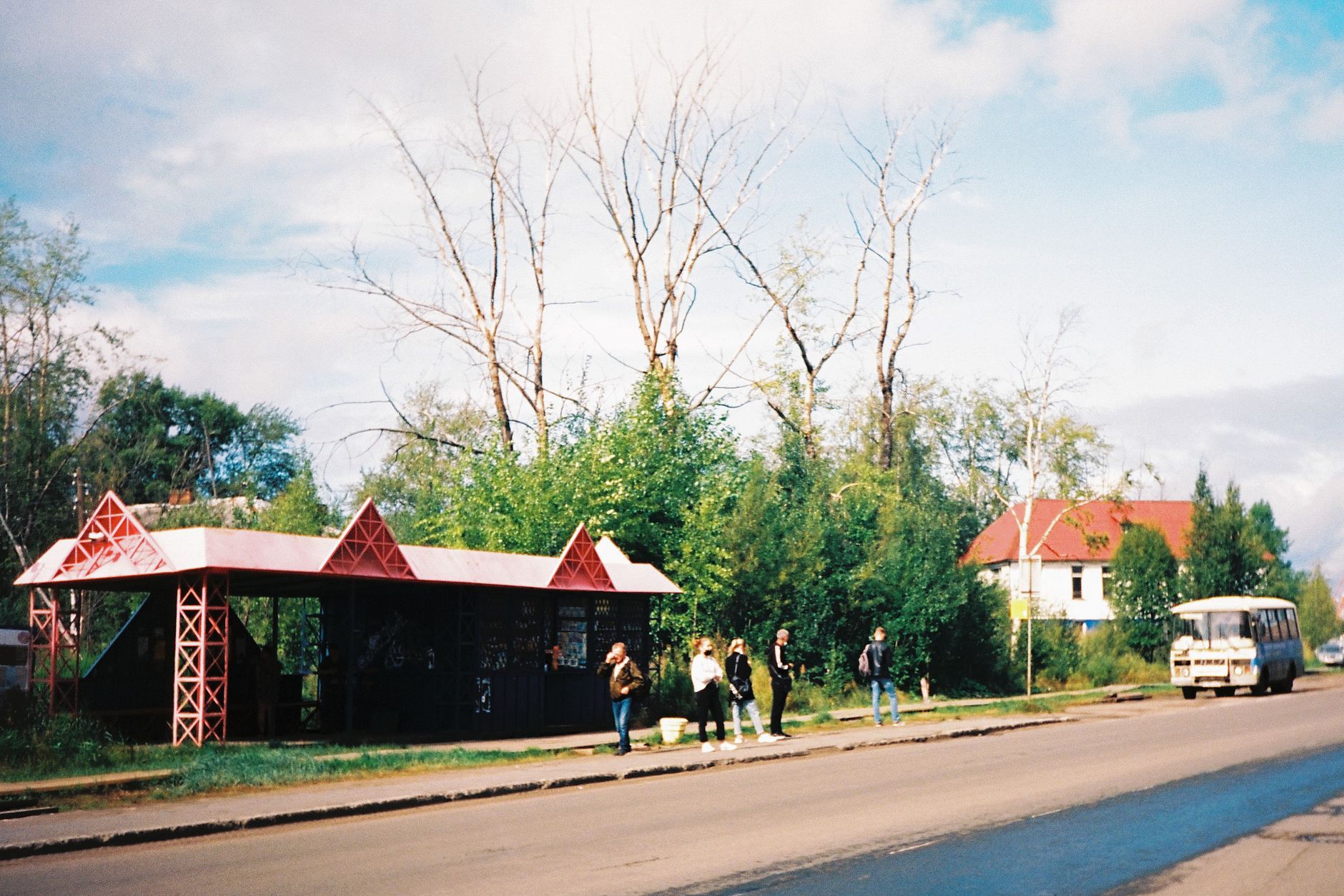 Quaint rural bus stop with people ready to catch a ride, surrounded by nature.